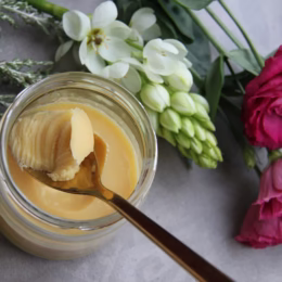 Pot de ghee maison doré posé sur une table fleurie, avec une cuillère un fond naturel