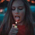 Jeune femme sur le point de mettre sa langue près d’une flamme, symbolisant un geste impulsif et automatique.