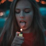 Jeune femme sur le point de mettre sa langue près d’une flamme, symbolisant un geste impulsif et automatique.