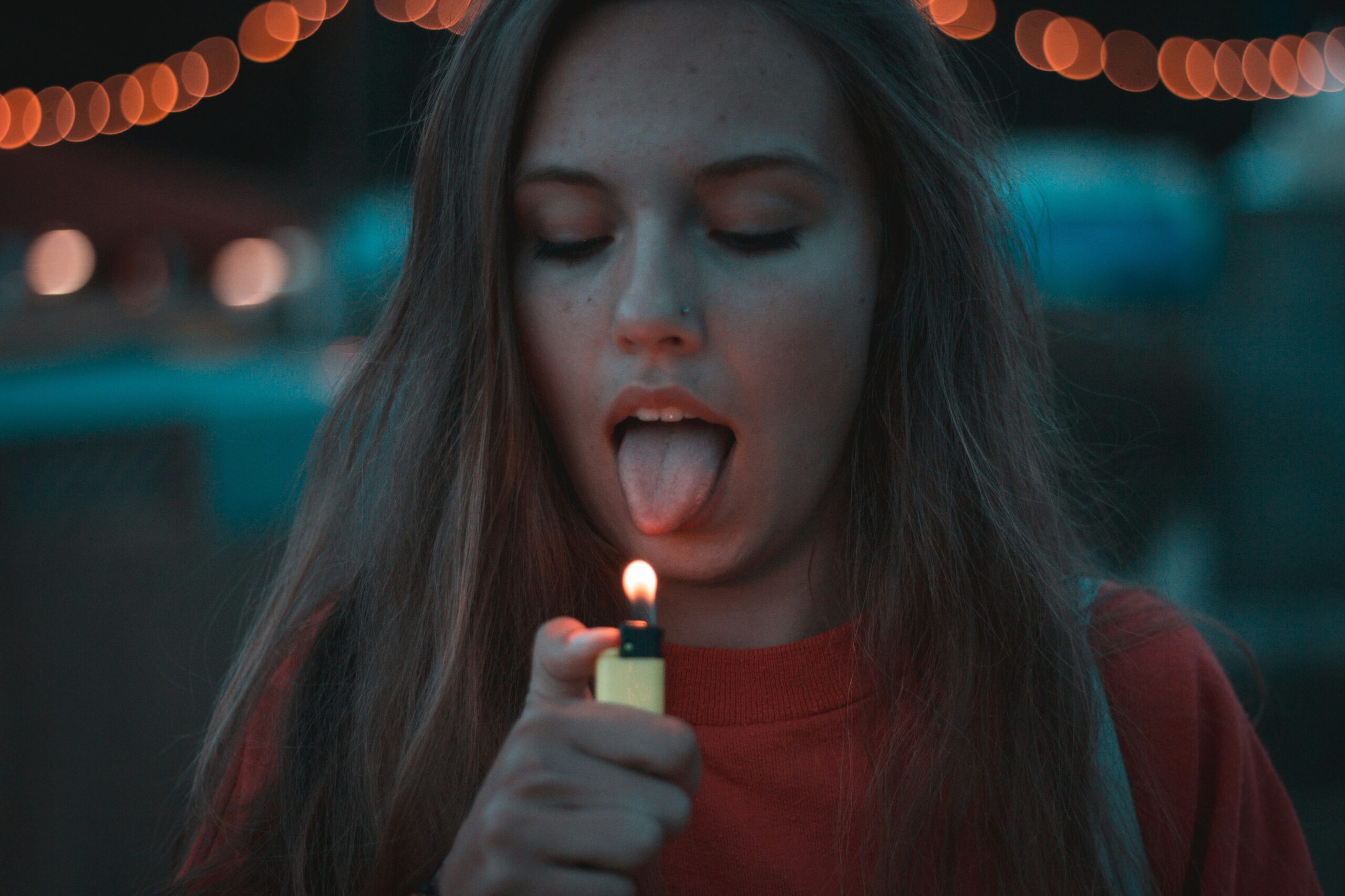 Jeune femme sur le point de mettre sa langue près d’une flamme, symbolisant un geste impulsif et automatique.