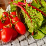 Tomates fraîches et feuilles de blette posées sur un torchon, représentant des aliments typiques du régime méditerranéen.