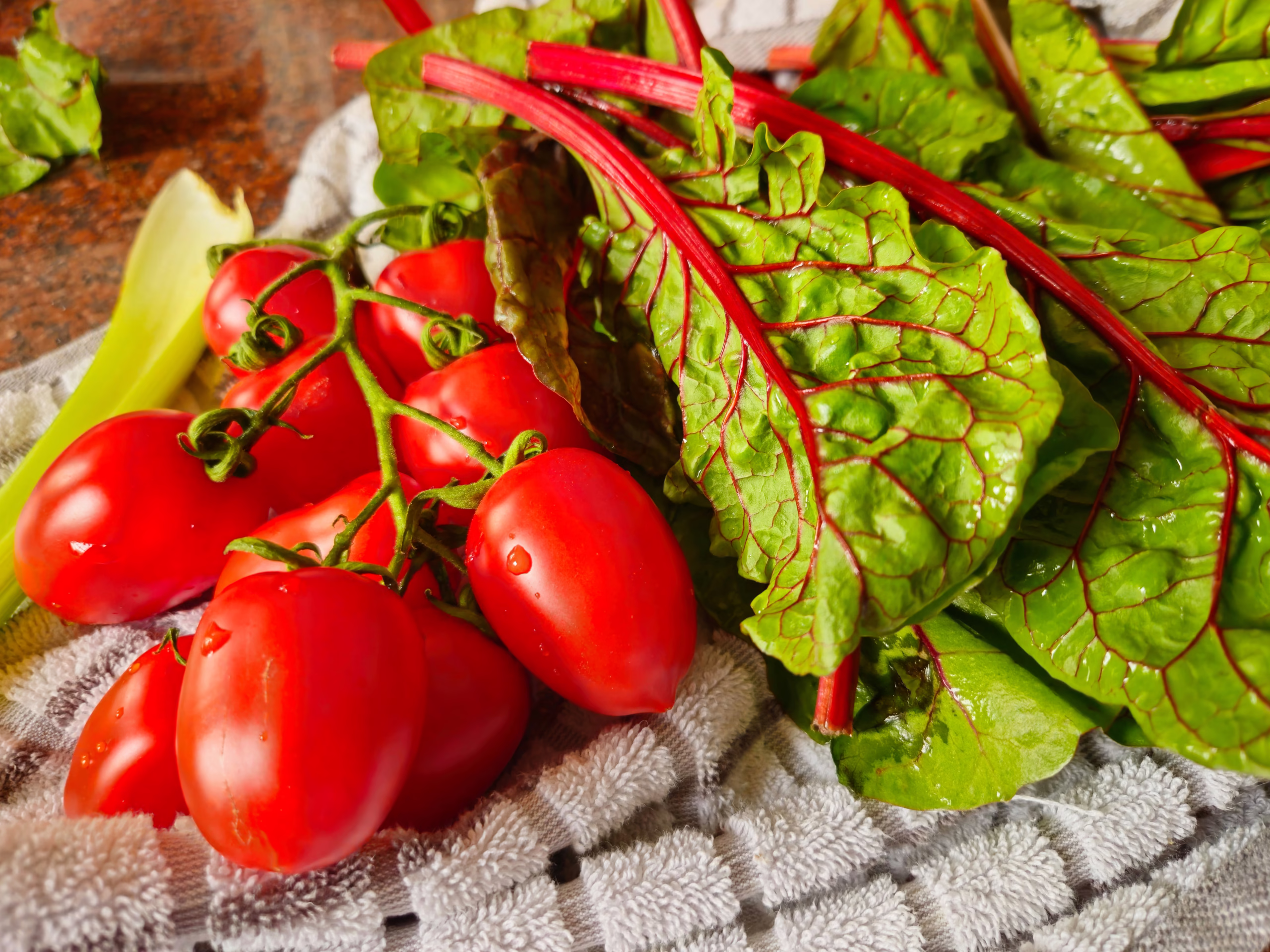 Tomates fraîches et feuilles de blette posées sur un torchon, représentant des aliments typiques du régime méditerranéen.