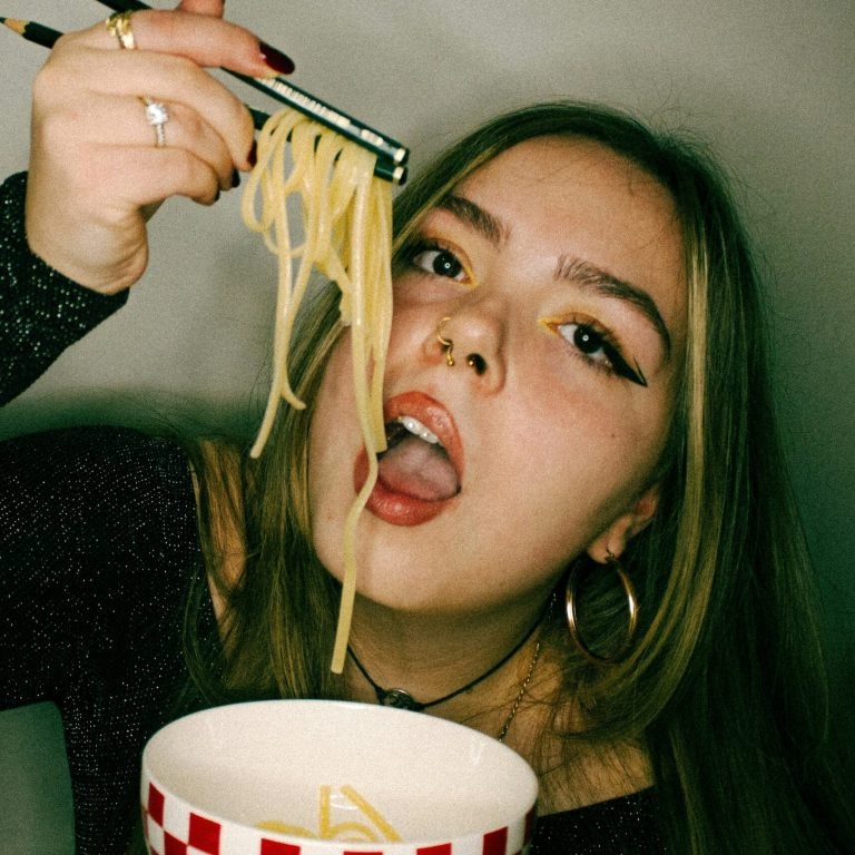 Jeune femme mangeant des pâtes avec des crayons, illustrant l’alimentation émotionnelle