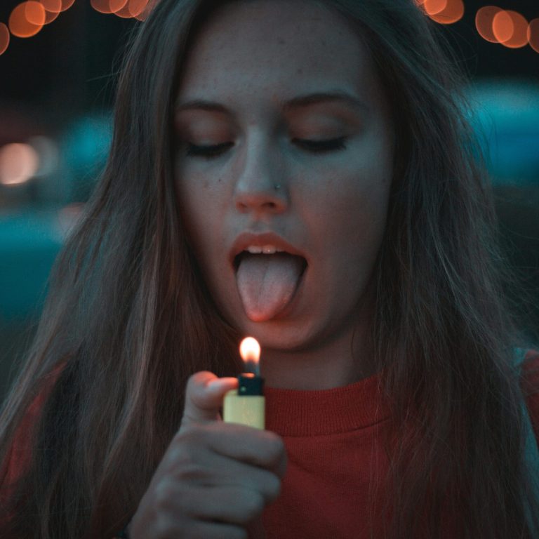 Jeune femme sur le point de mettre sa langue près d’une flamme, symbolisant un geste impulsif et automatique.