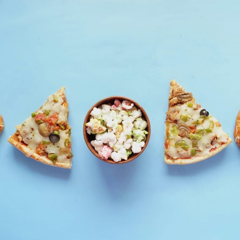 Assortiment de junk food illustrant les envies incontrôlées : pizza, pâtisseries sucrées et pop-corn colorés