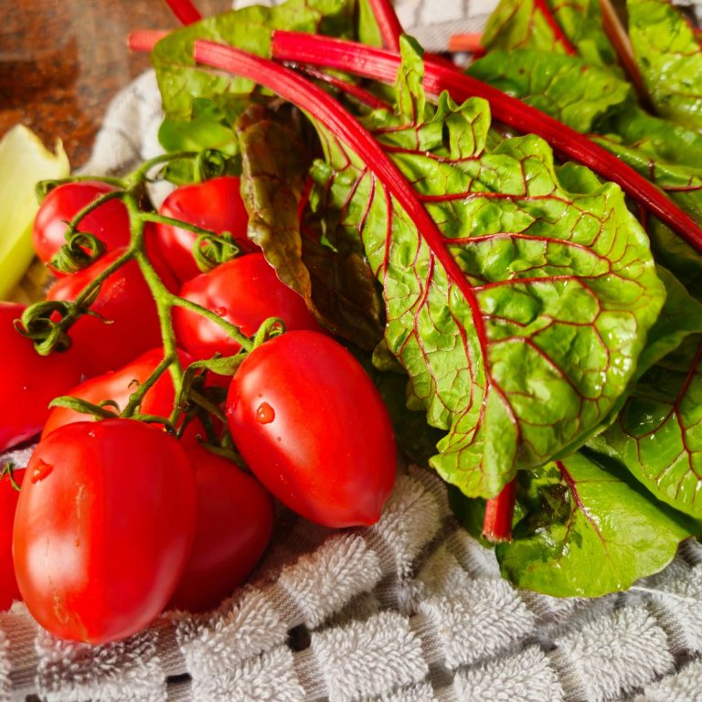 Tomates fraîches et feuilles de blette posées sur un torchon, représentant des aliments typiques du régime méditerranéen.